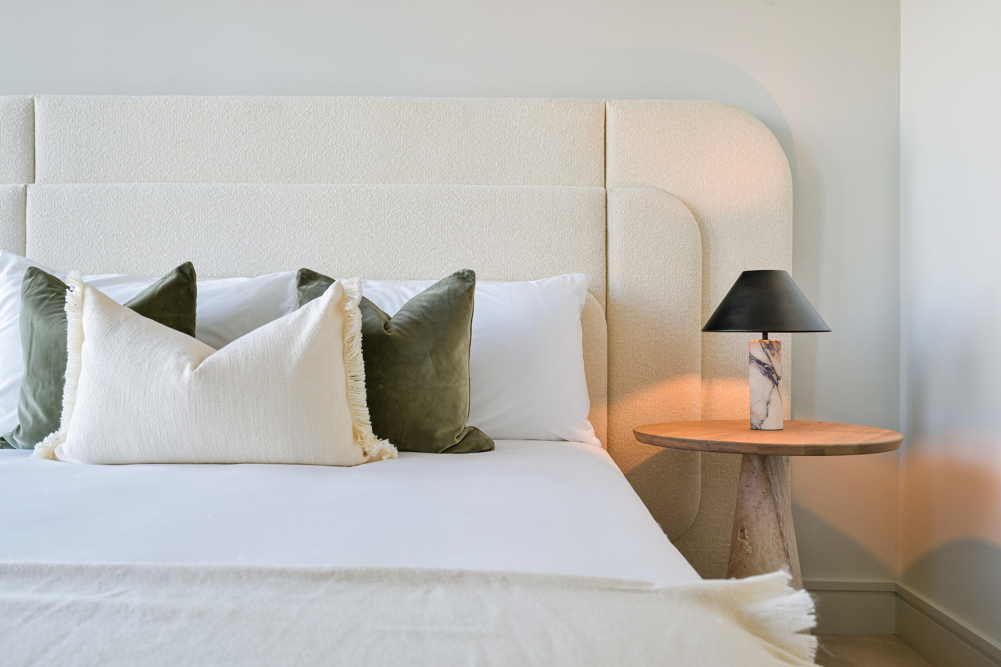 A bedroom in a Sky Residence with a bouclé headboard and marble lamp
